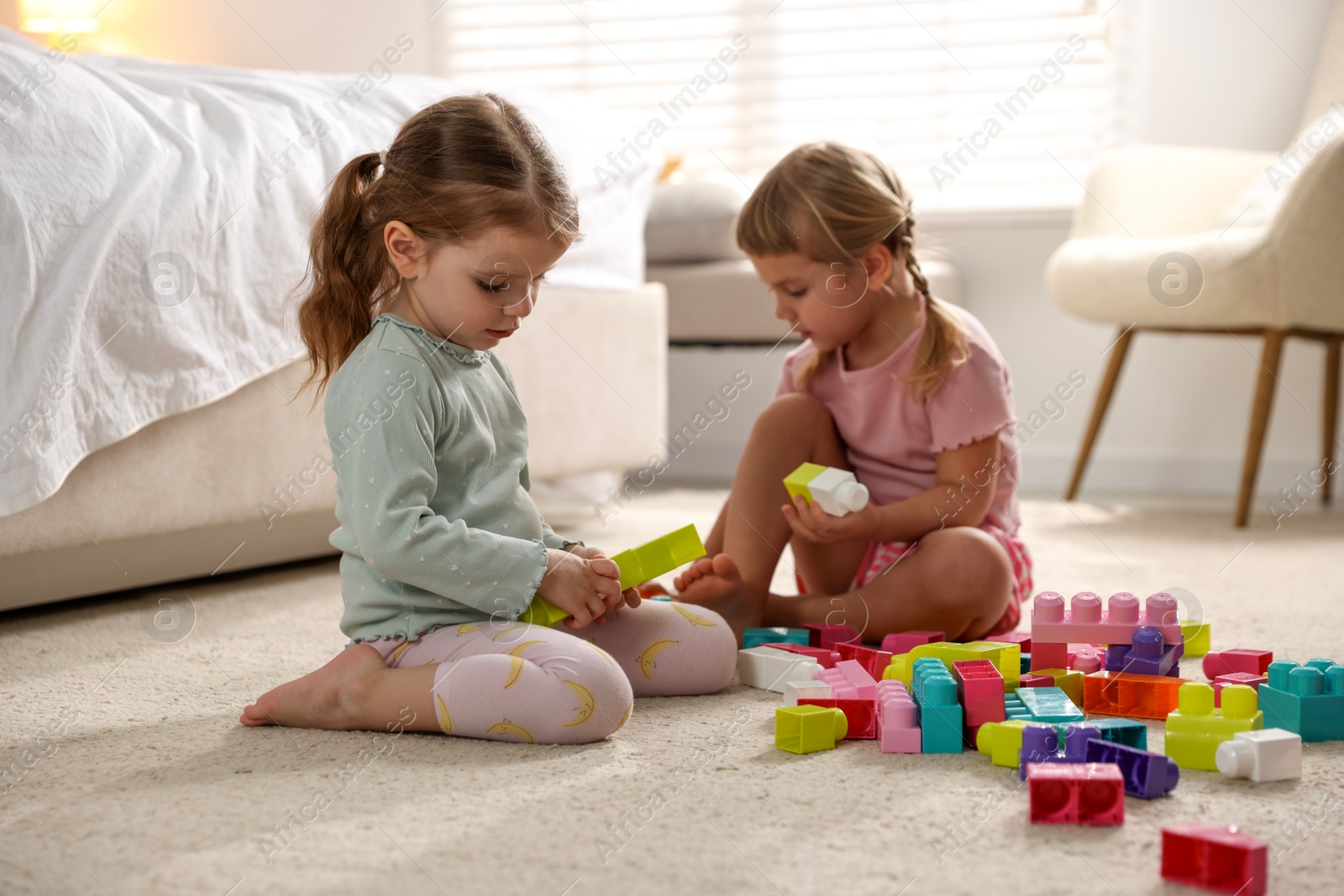 Photo of Cute little sisters playing with colorful building blocks on floor at home