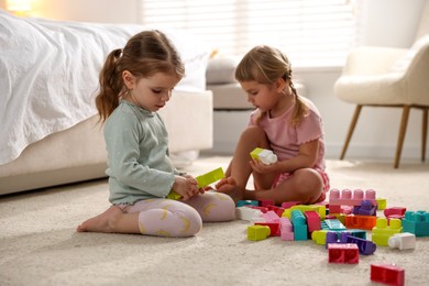 Photo of Cute little sisters playing with colorful building blocks on floor at home