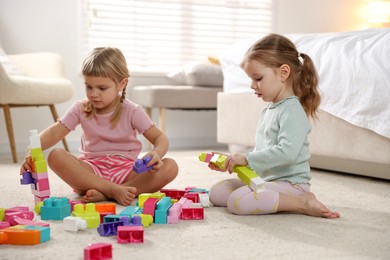 Photo of Cute little sisters playing with colorful building blocks on floor at home