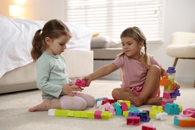 Photo of Cute little sisters playing with colorful building blocks on floor at home