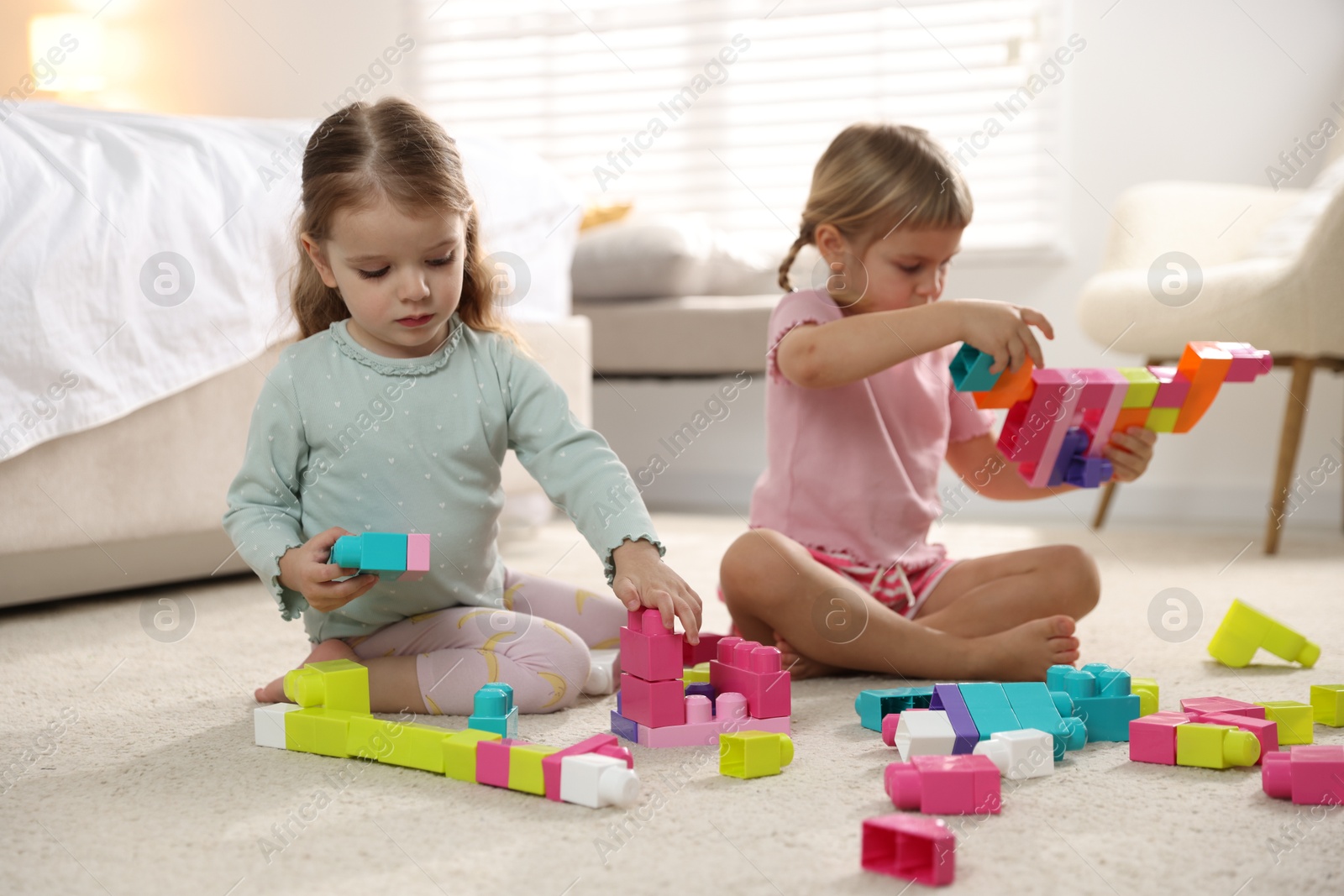 Photo of Cute little sisters playing with colorful building blocks on floor at home