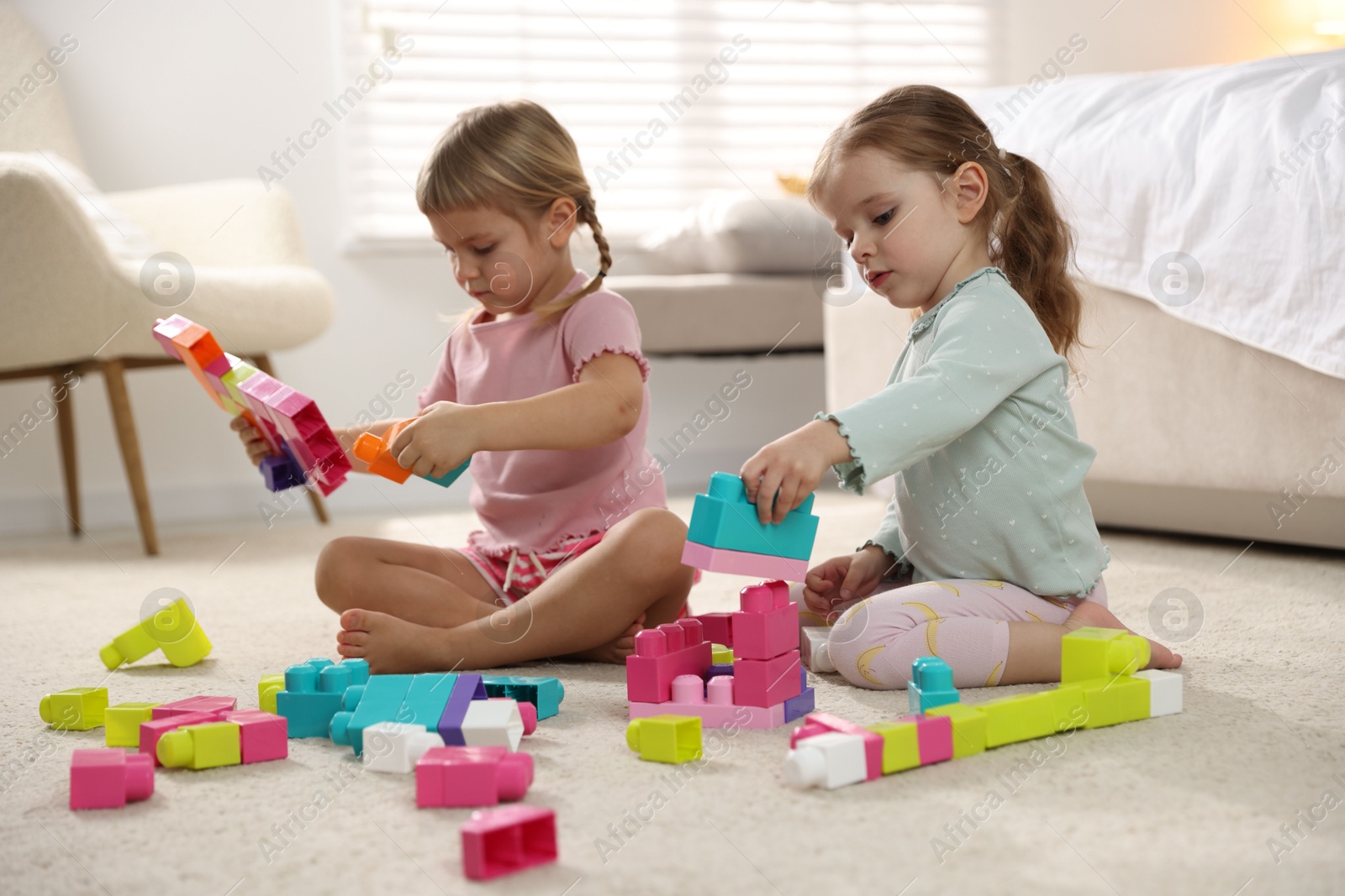 Photo of Cute little sisters playing with colorful building blocks on floor at home