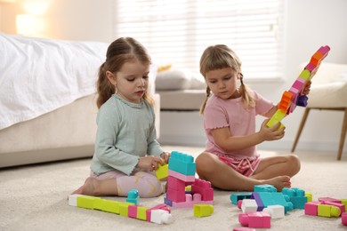 Photo of Cute little sisters playing with colorful building blocks on floor at home