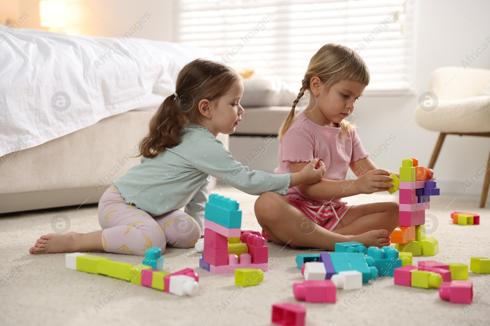 Photo of Cute little sisters playing with colorful building blocks on floor at home