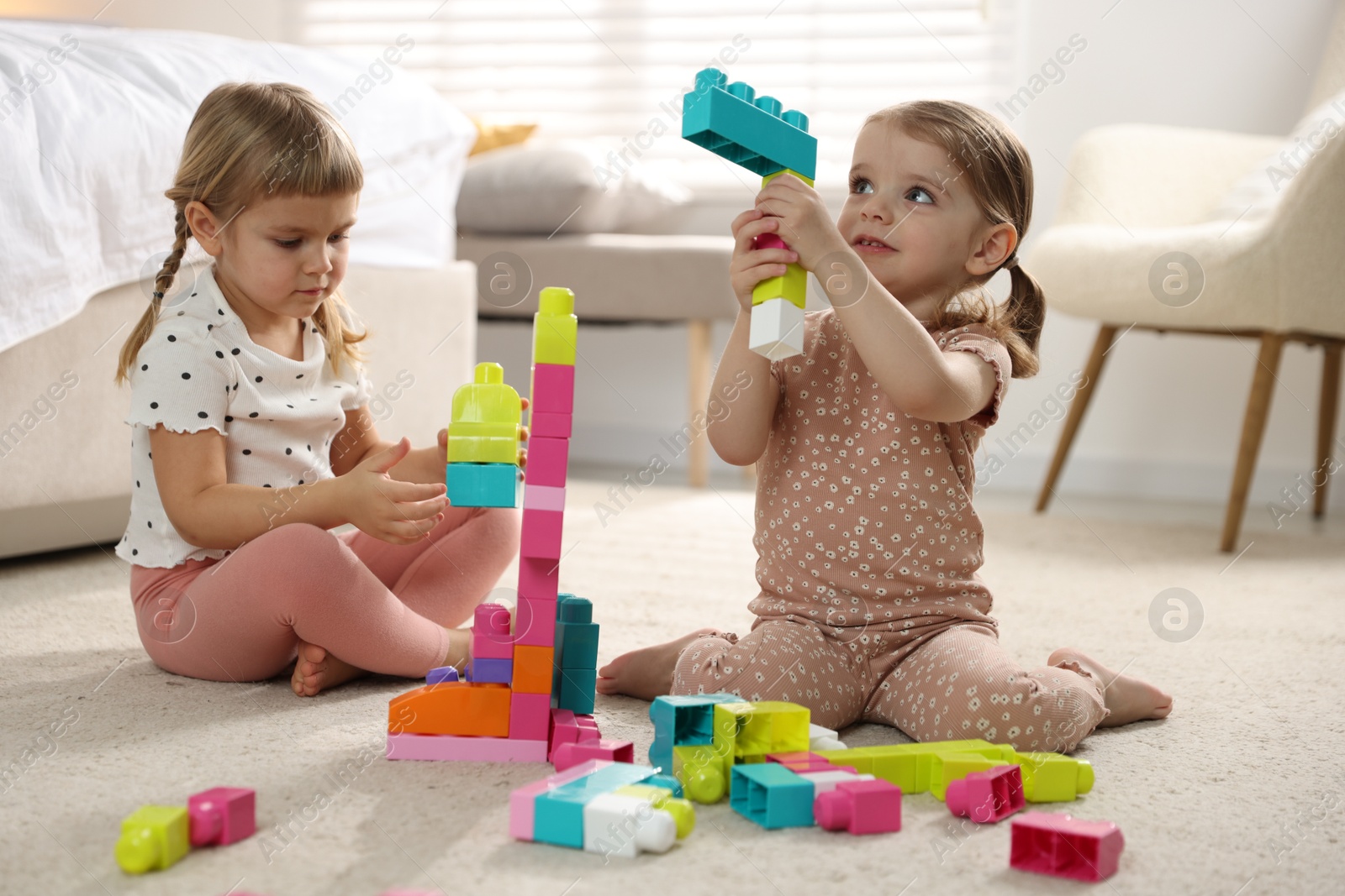 Photo of Cute little sisters playing with colorful building blocks on floor at home