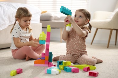 Photo of Cute little sisters playing with colorful building blocks on floor at home