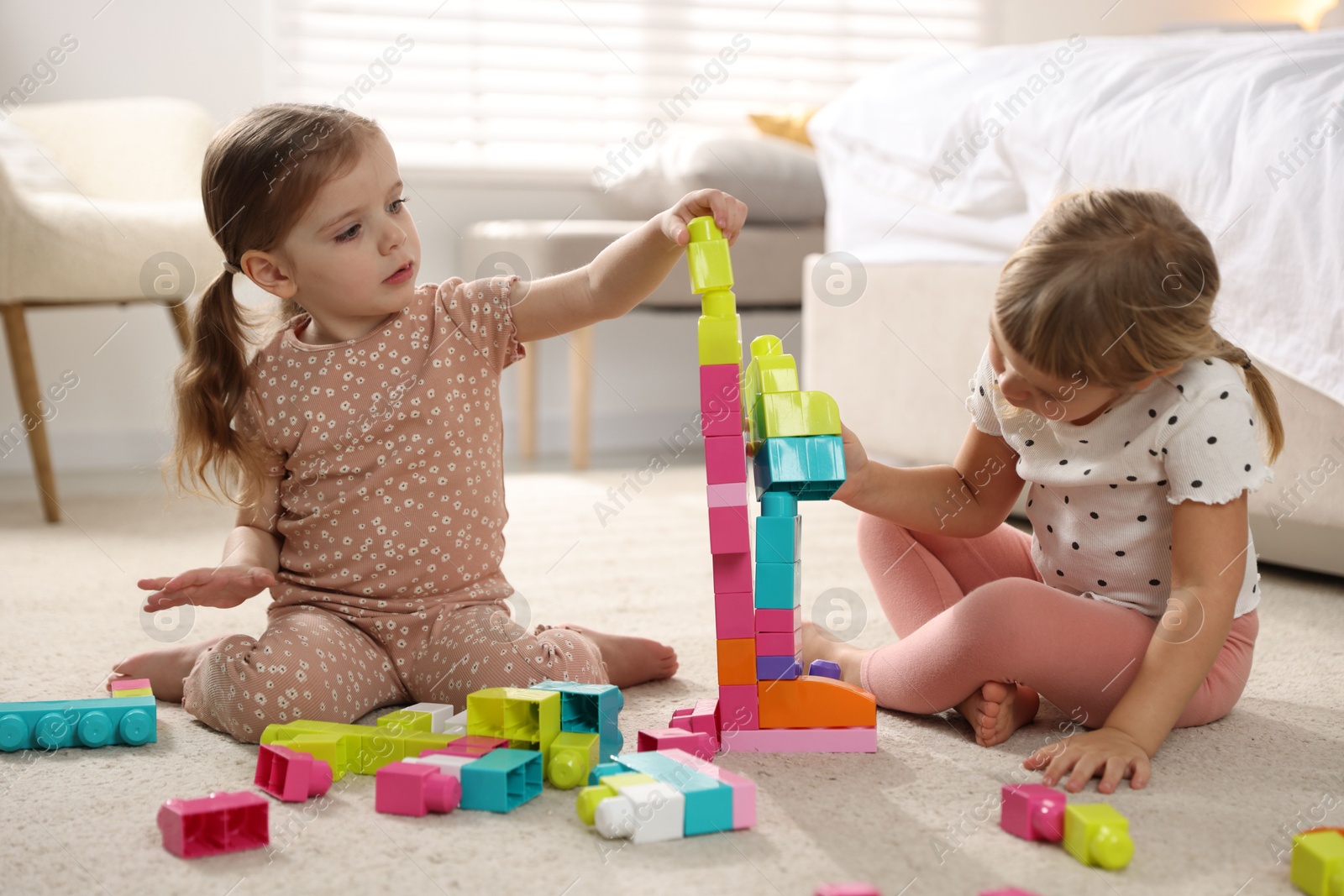 Photo of Cute little sisters playing with colorful building blocks on floor at home