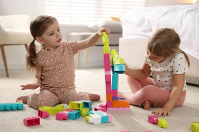 Photo of Cute little sisters playing with colorful building blocks on floor at home