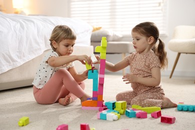 Photo of Cute little sisters playing with colorful building blocks on floor at home