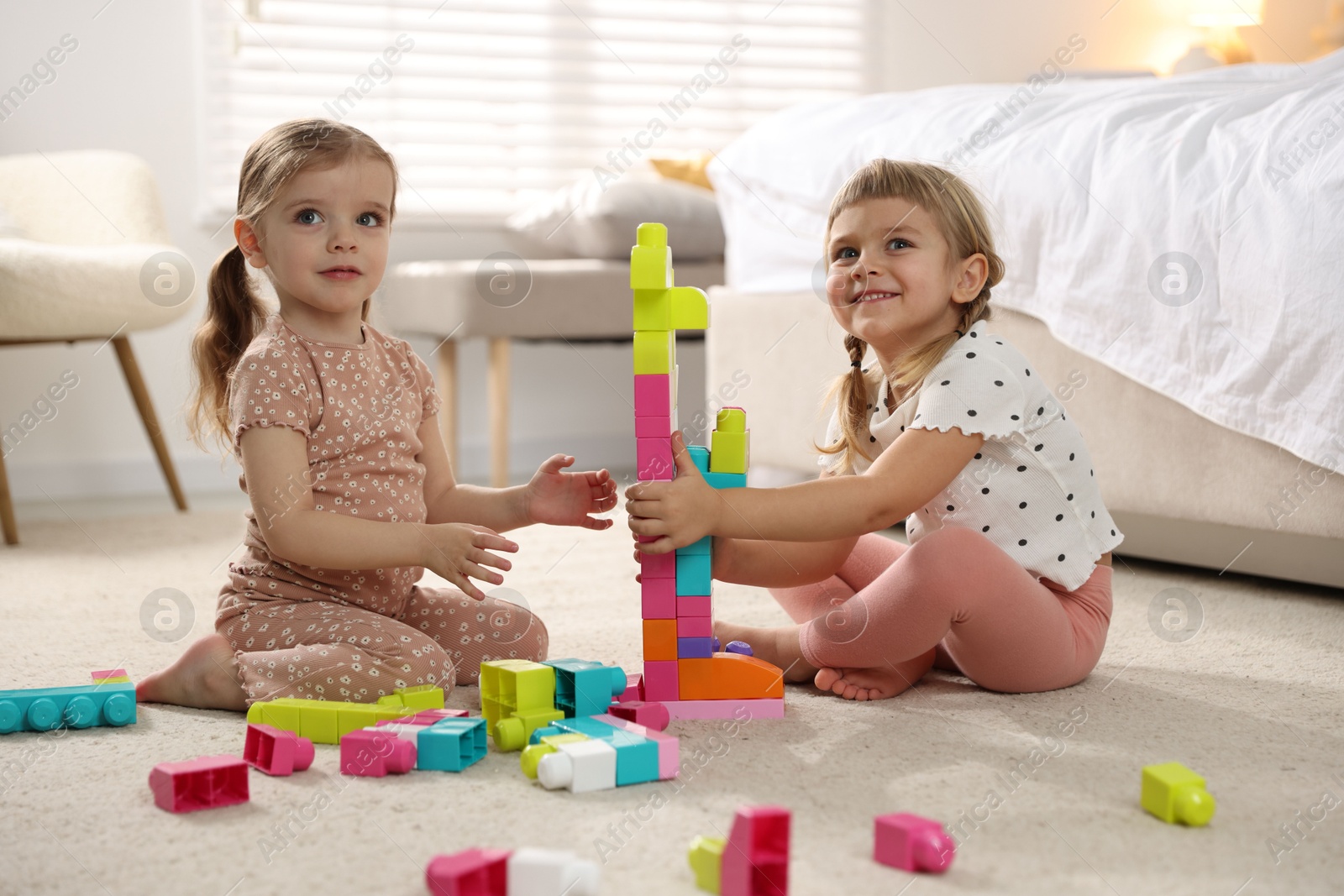 Photo of Cute little sisters playing with colorful building blocks on floor at home