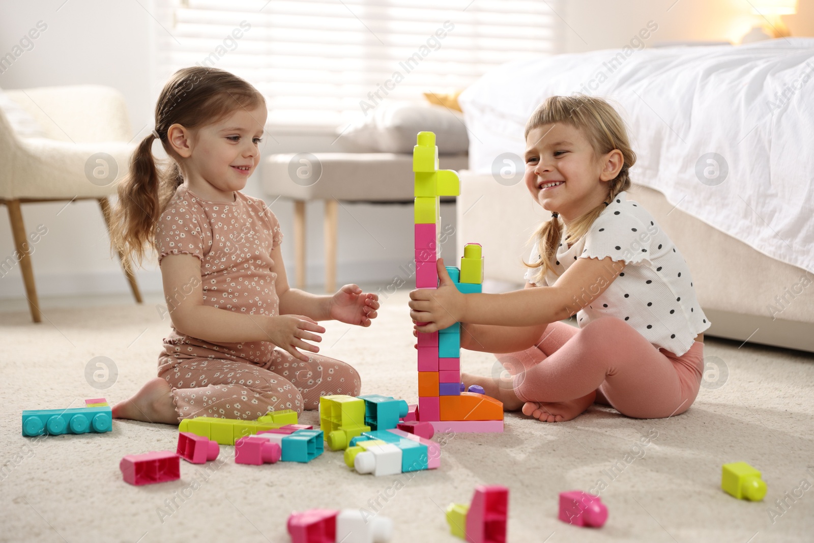 Photo of Cute little sisters playing with colorful building blocks on floor at home