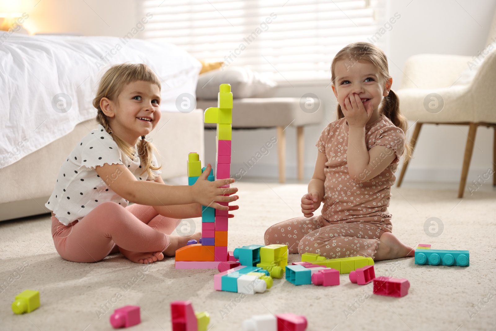 Photo of Cute little sisters playing with colorful building blocks on floor at home