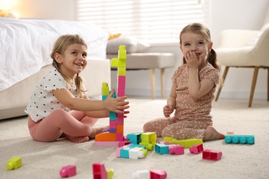 Cute little sisters playing with colorful building blocks on floor at home