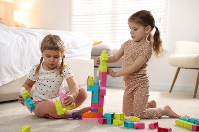 Photo of Cute little sisters playing with colorful building blocks on floor at home