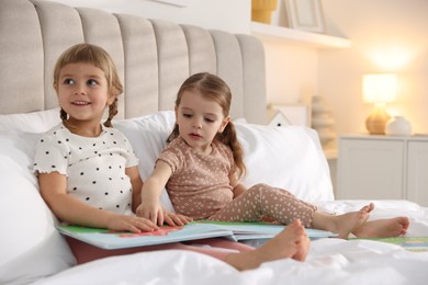 Photo of Cute little sisters reading book together in bed at home