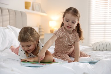 Photo of Cute little sisters reading book together on bed at home