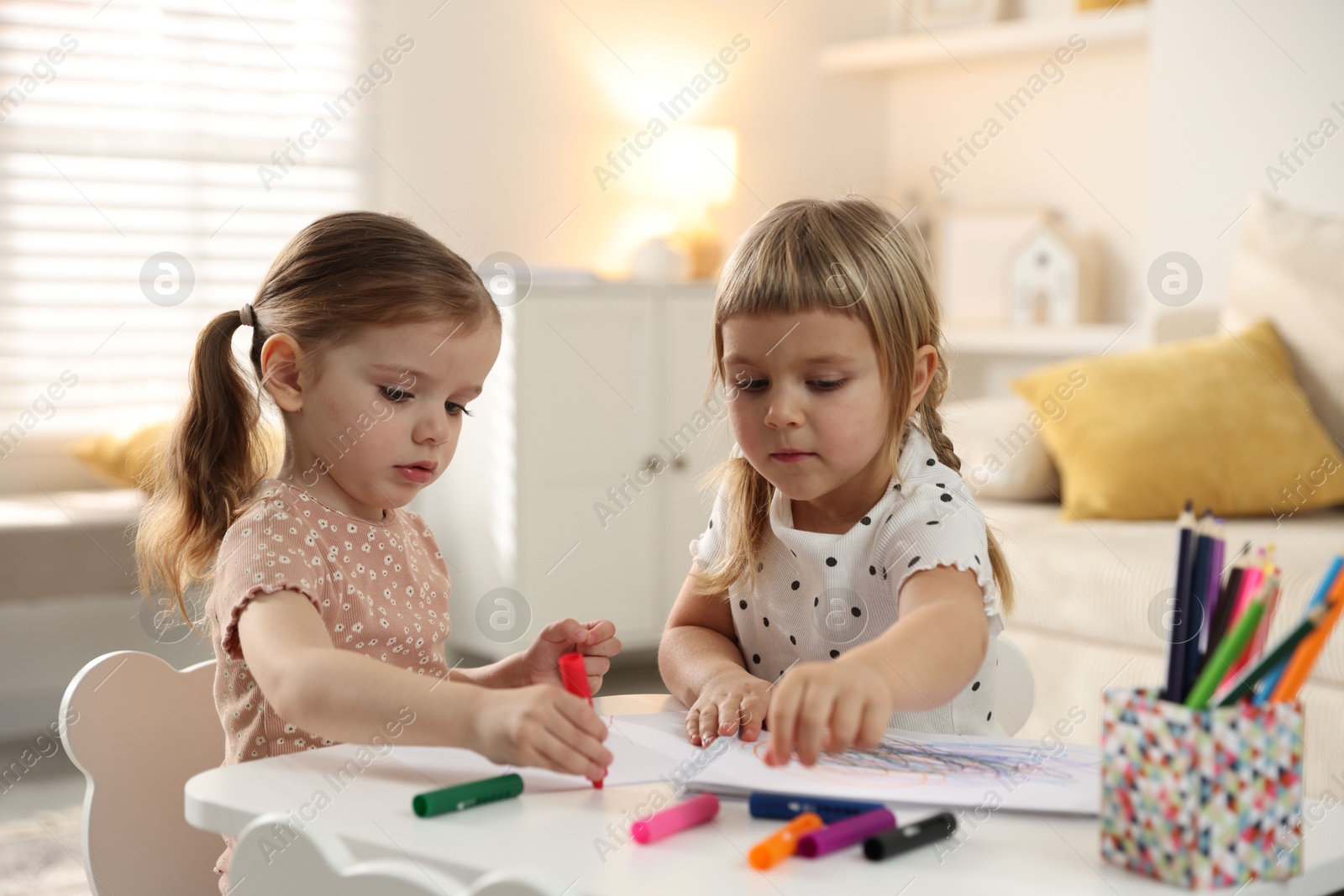 Photo of Cute little sisters drawing at white table in room