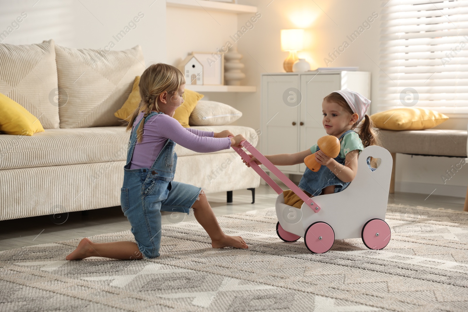 Photo of Cute little sisters playing with toy stroller at home