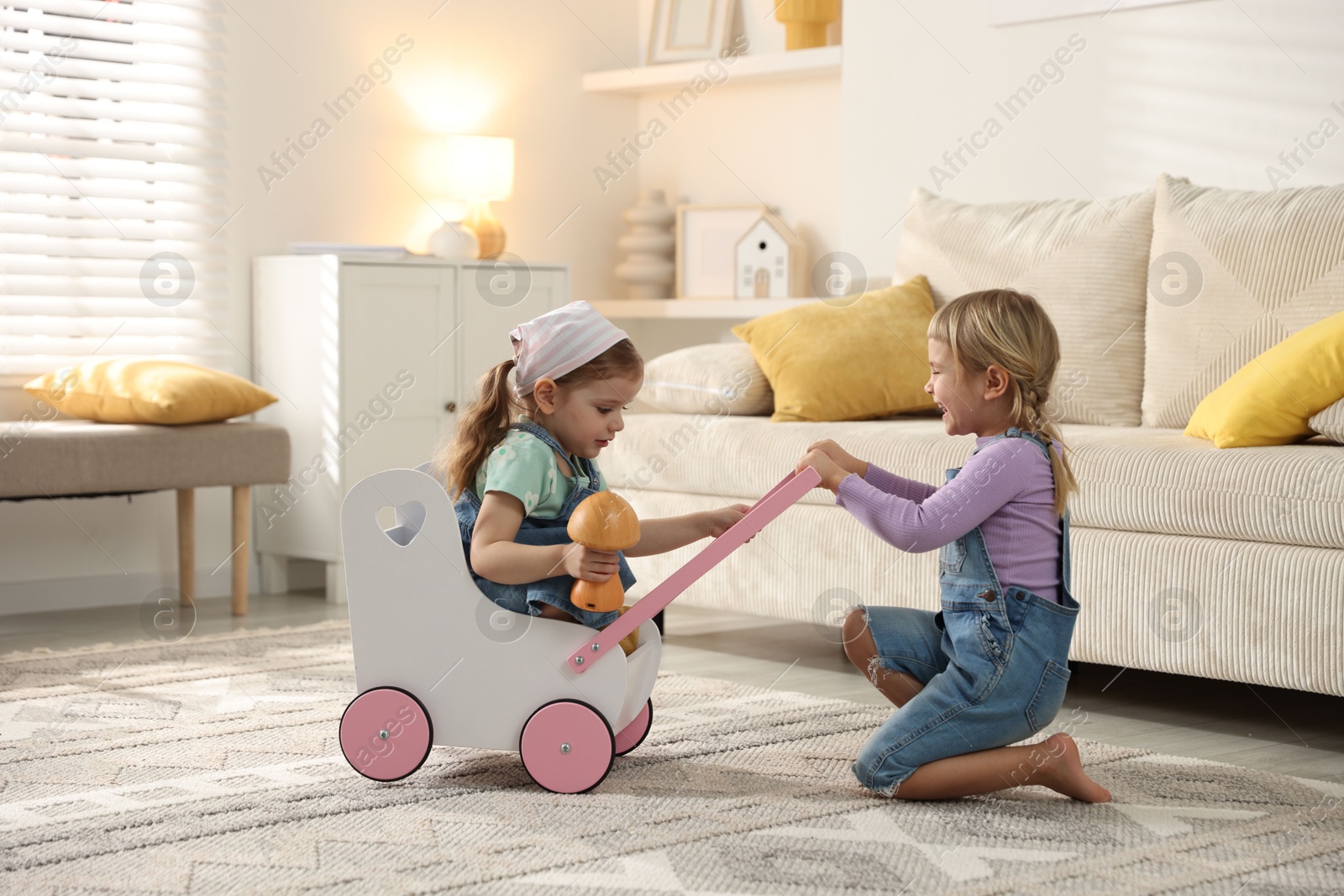 Photo of Cute little sisters playing with toy stroller at home