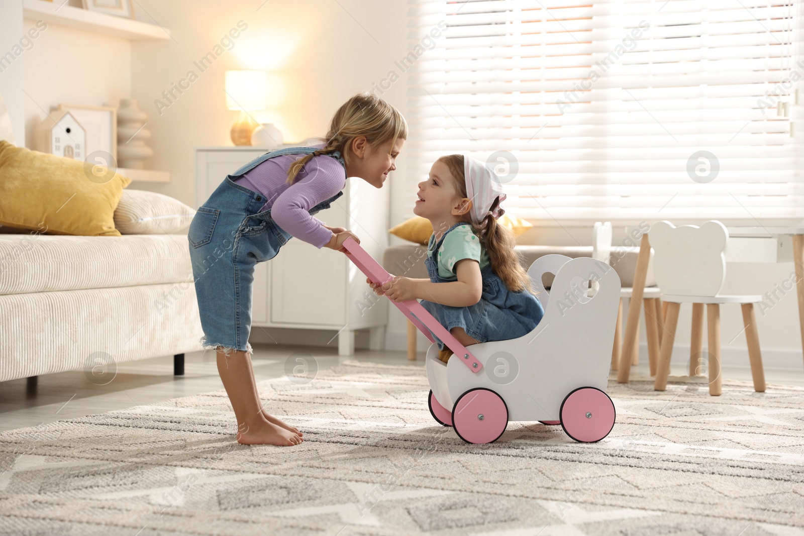 Photo of Cute little sisters playing with toy stroller at home