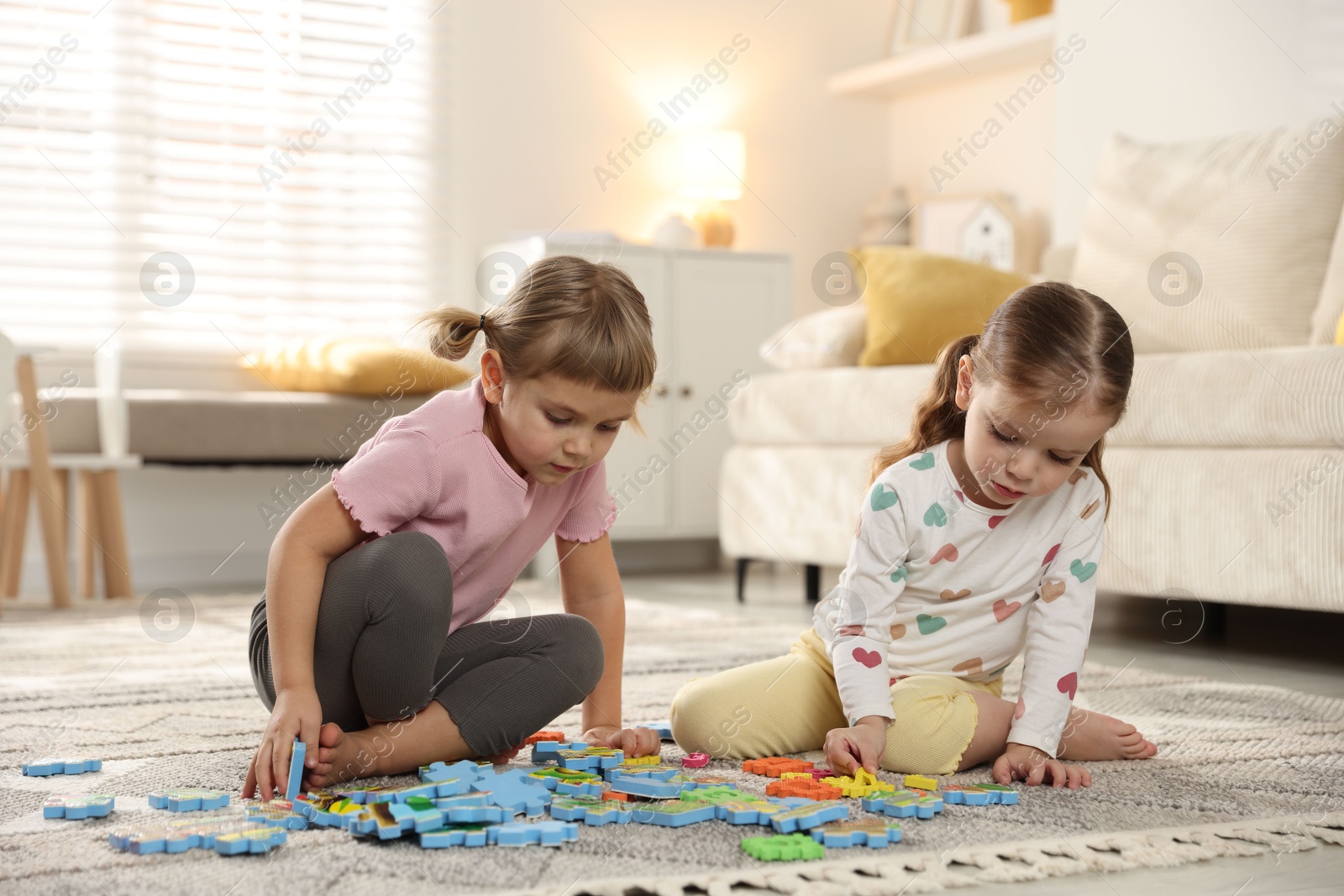 Photo of Cute little sisters playing with puzzles on floor at home