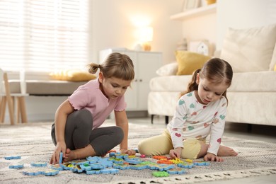 Photo of Cute little sisters playing with puzzles on floor at home