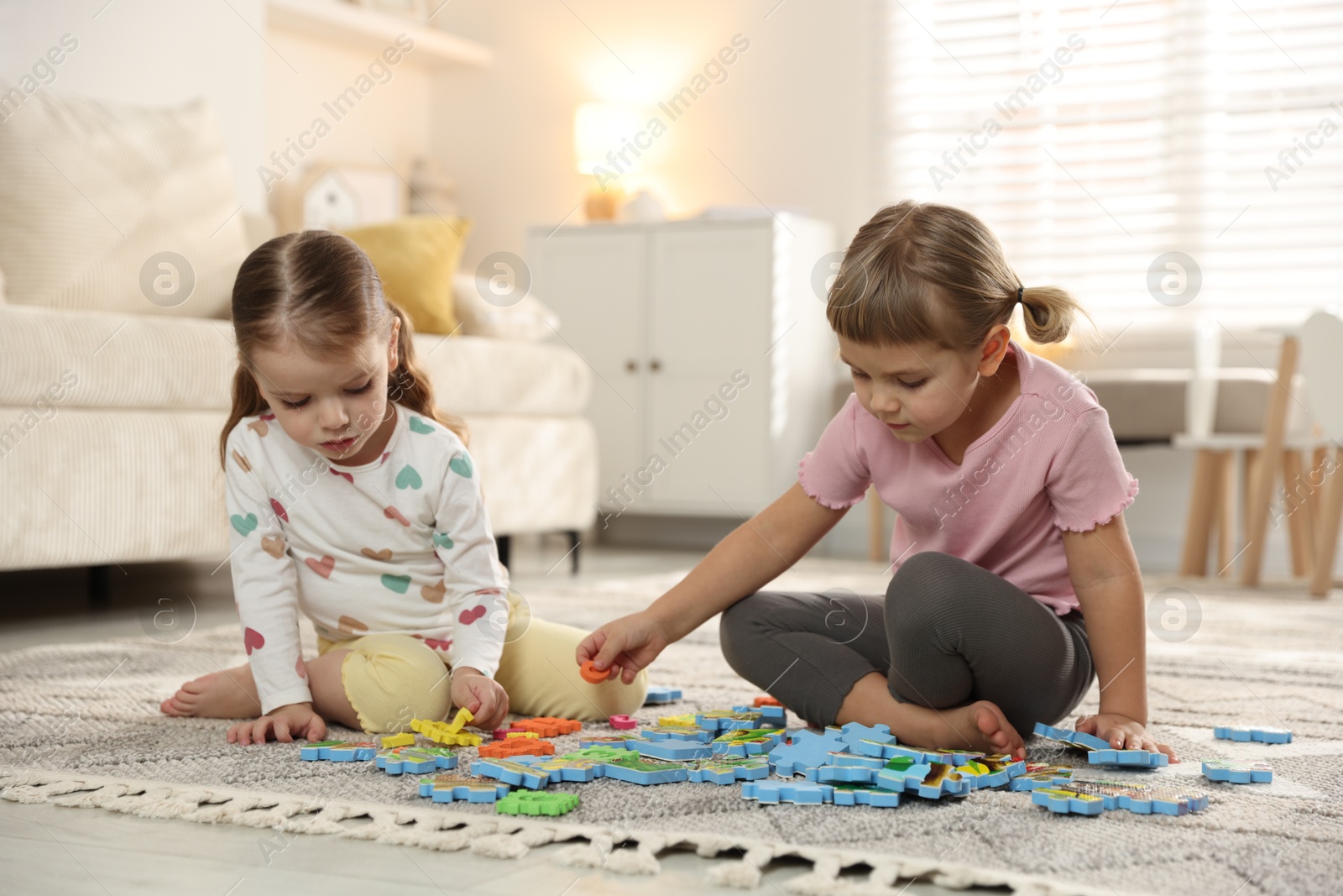 Photo of Cute little sisters playing with puzzles on floor at home