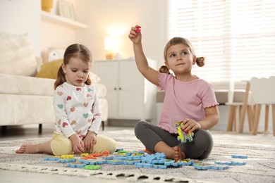 Photo of Cute little sisters playing with puzzles on floor at home