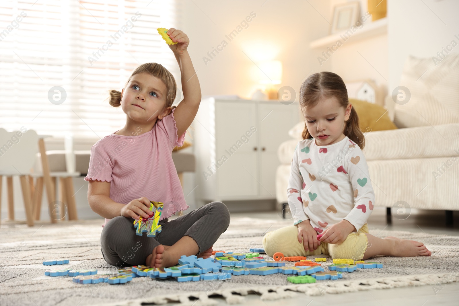 Photo of Cute little sisters playing with puzzles on floor at home