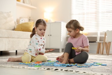 Photo of Cute little sisters playing with puzzles on floor at home