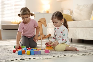 Photo of Cute little sisters playing with toy pyramids on floor at home