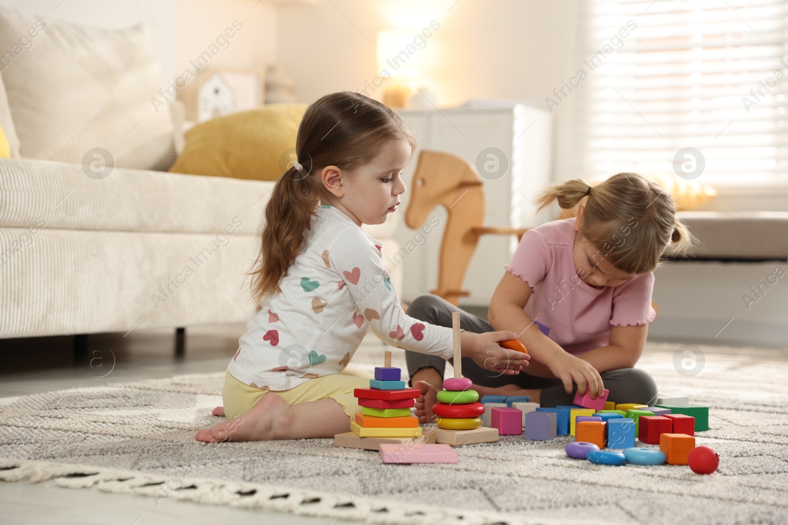 Photo of Cute little sisters playing with toy pyramids on floor at home