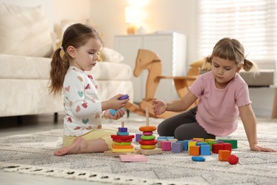 Photo of Cute little sisters playing with toy pyramids on floor at home