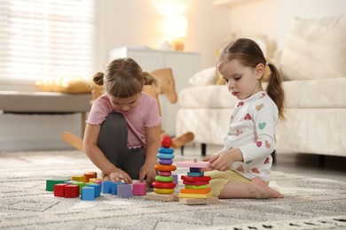 Photo of Cute little sisters playing with toy pyramids on floor at home