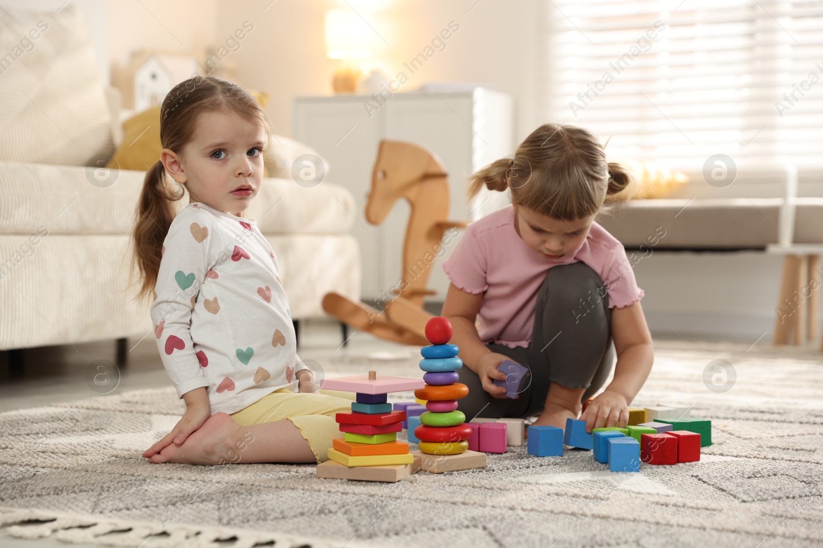 Photo of Cute little sisters playing with toy pyramids on floor at home