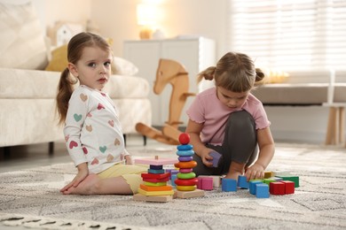 Photo of Cute little sisters playing with toy pyramids on floor at home