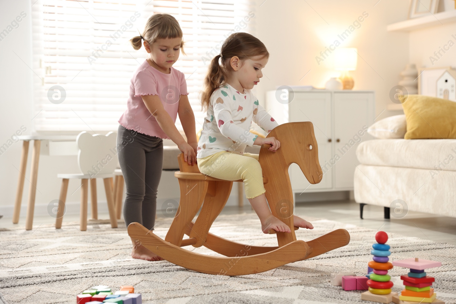 Photo of Cute little sisters playing with wooden rocking horse at home