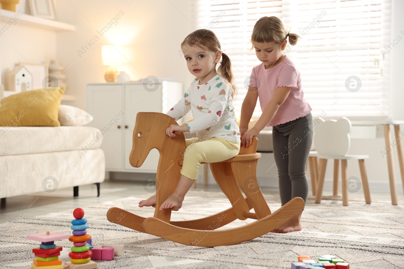 Photo of Cute little sisters playing with wooden rocking horse at home