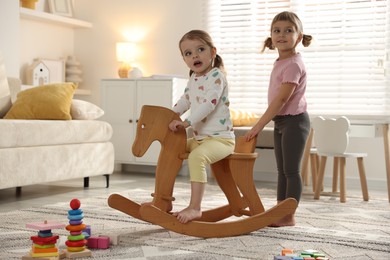 Photo of Cute little sisters playing with wooden rocking horse at home