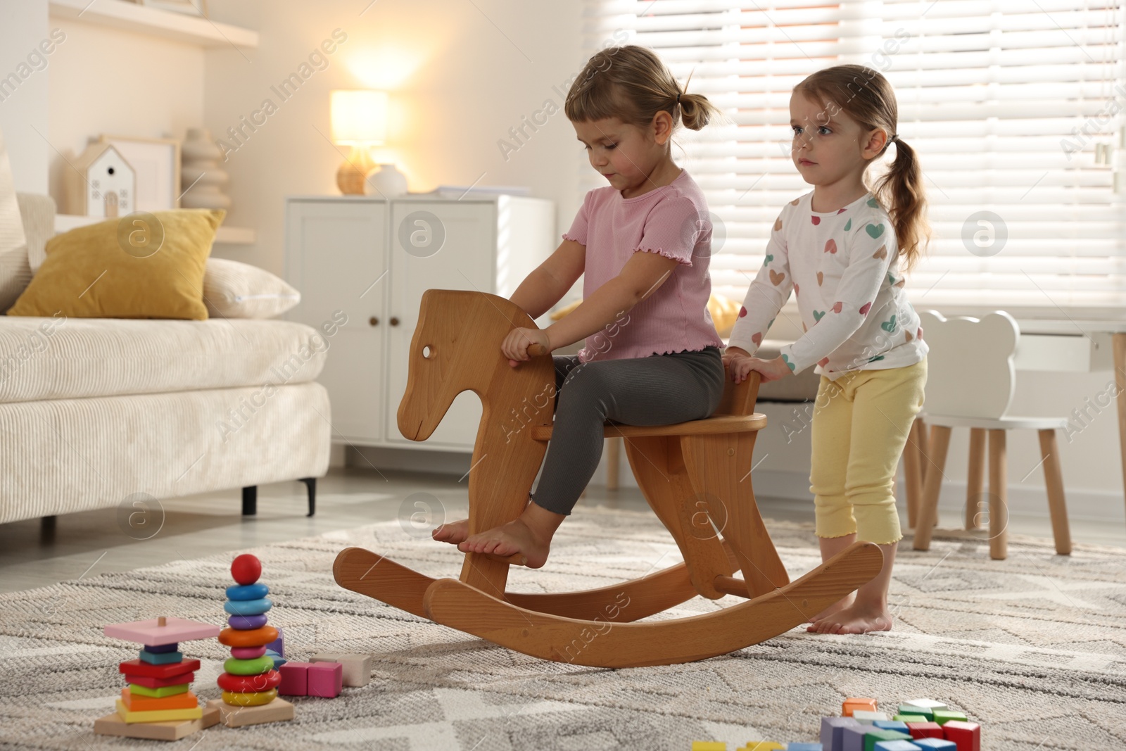 Photo of Cute little sisters playing with wooden rocking horse at home