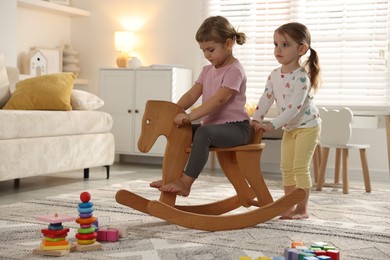 Photo of Cute little sisters playing with wooden rocking horse at home