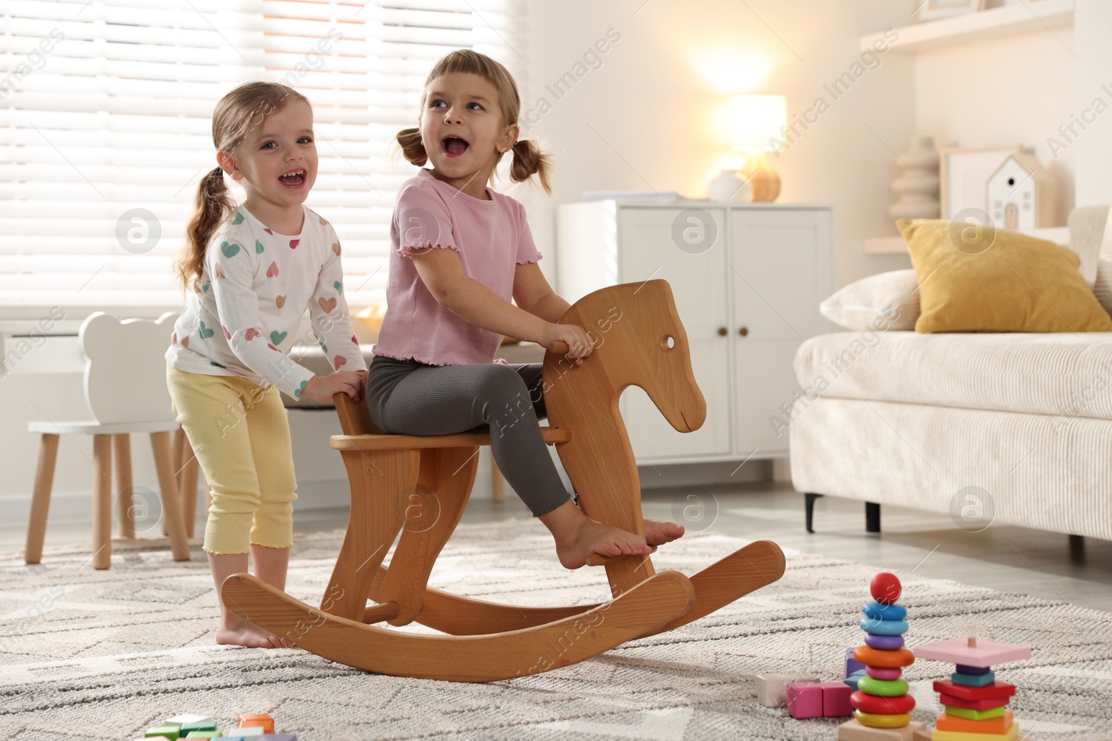 Photo of Cute little sisters playing with wooden rocking horse at home