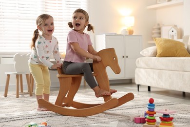 Photo of Cute little sisters playing with wooden rocking horse at home