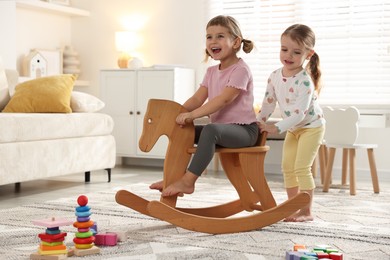 Photo of Cute little sisters playing with wooden rocking horse at home