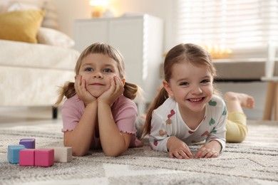 Photo of Cute little sisters lying on floor at home