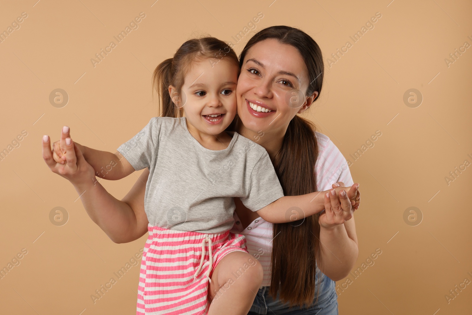 Photo of Portrait of happy mother and her cute little daughter on beige background