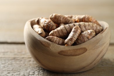 Photo of Raw turmeric roots in bowl on wooden table, closeup