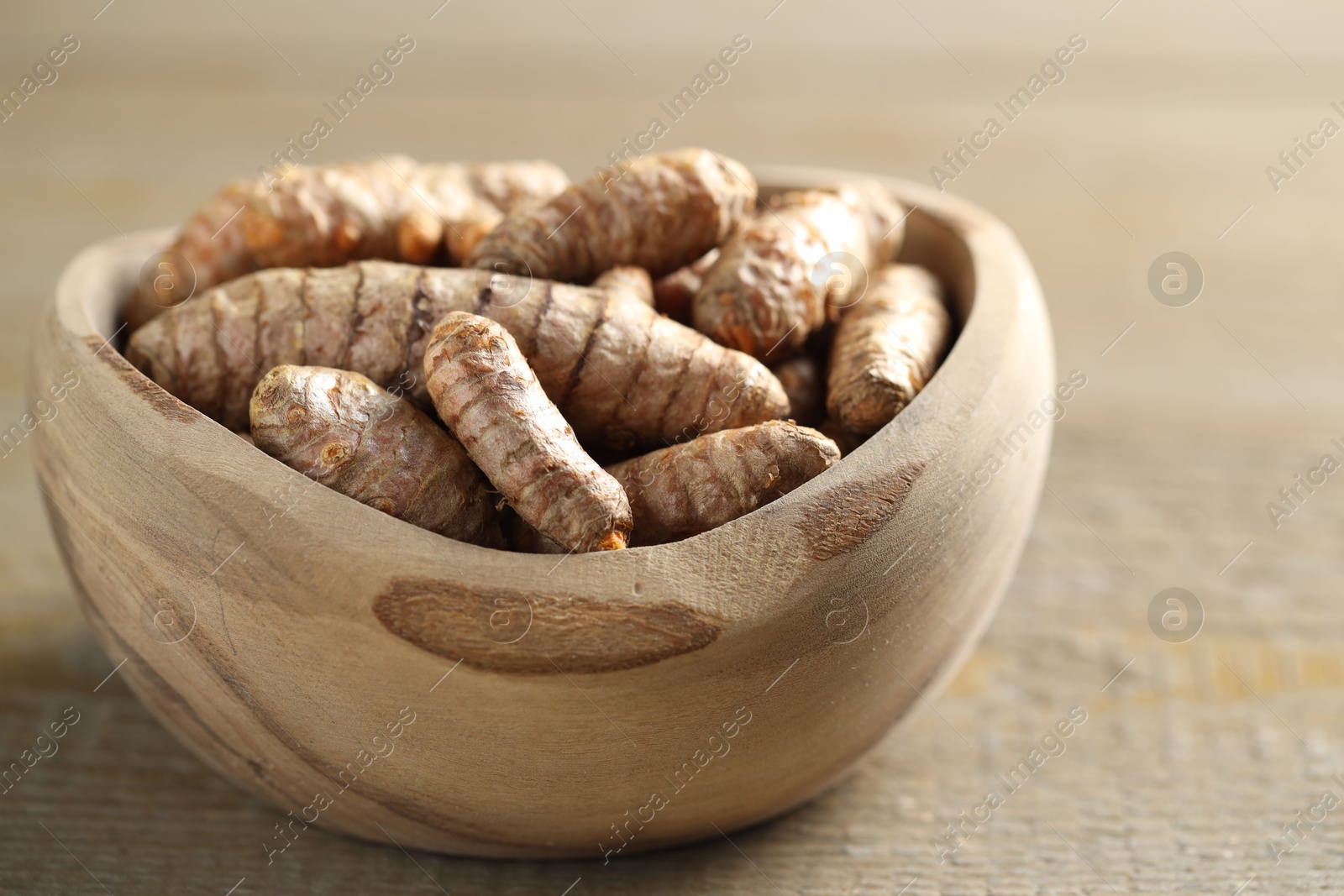 Photo of Raw turmeric roots in bowl on wooden table, closeup