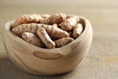 Photo of Raw turmeric roots in bowl on wooden table, closeup