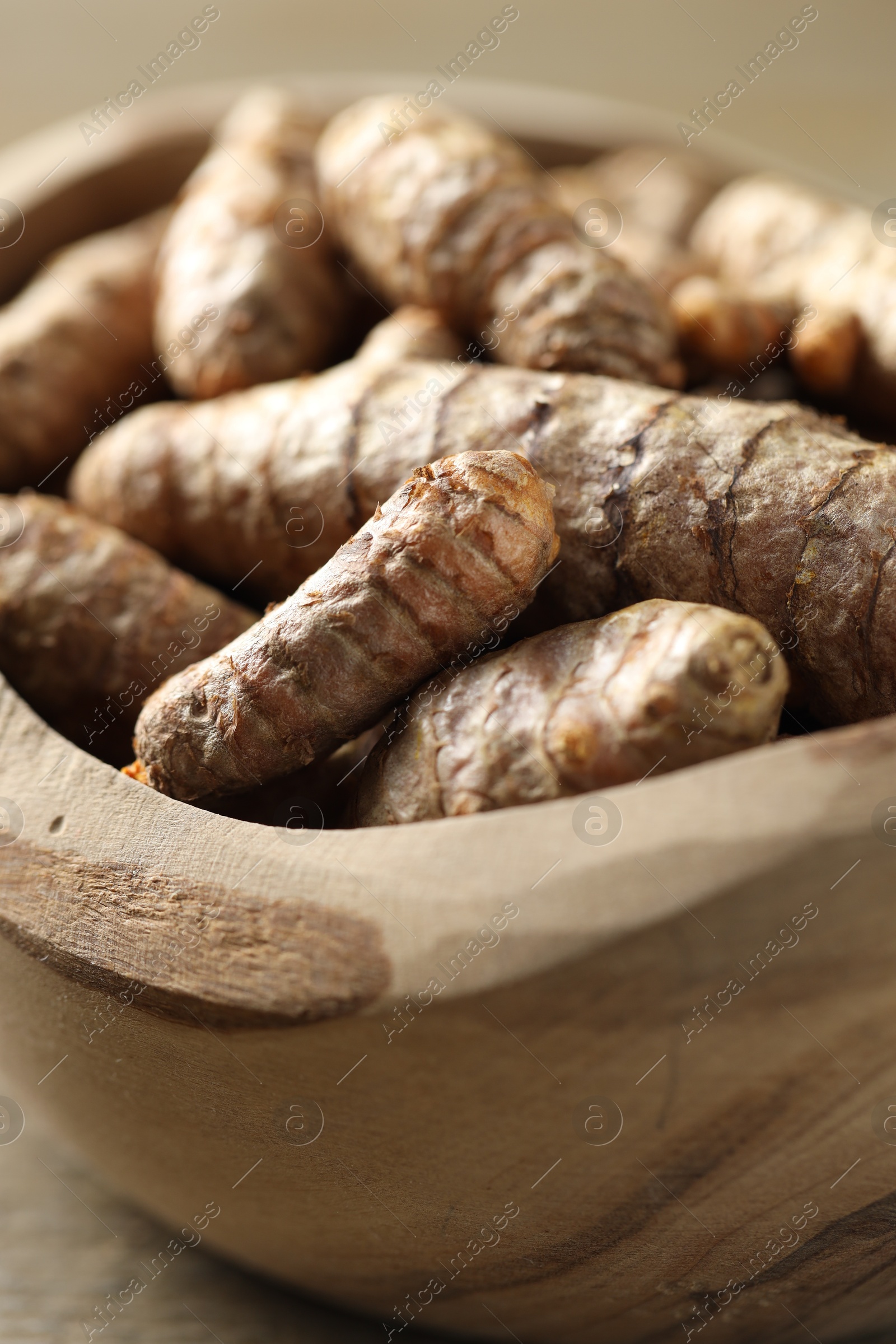 Photo of Raw turmeric roots in bowl on table, closeup